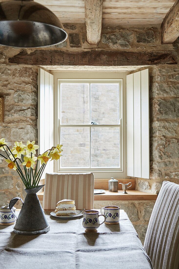 Daffodils in jug on dining table with sponge cake and mugs in Grade II listed Tudor bastle Northumberland UK