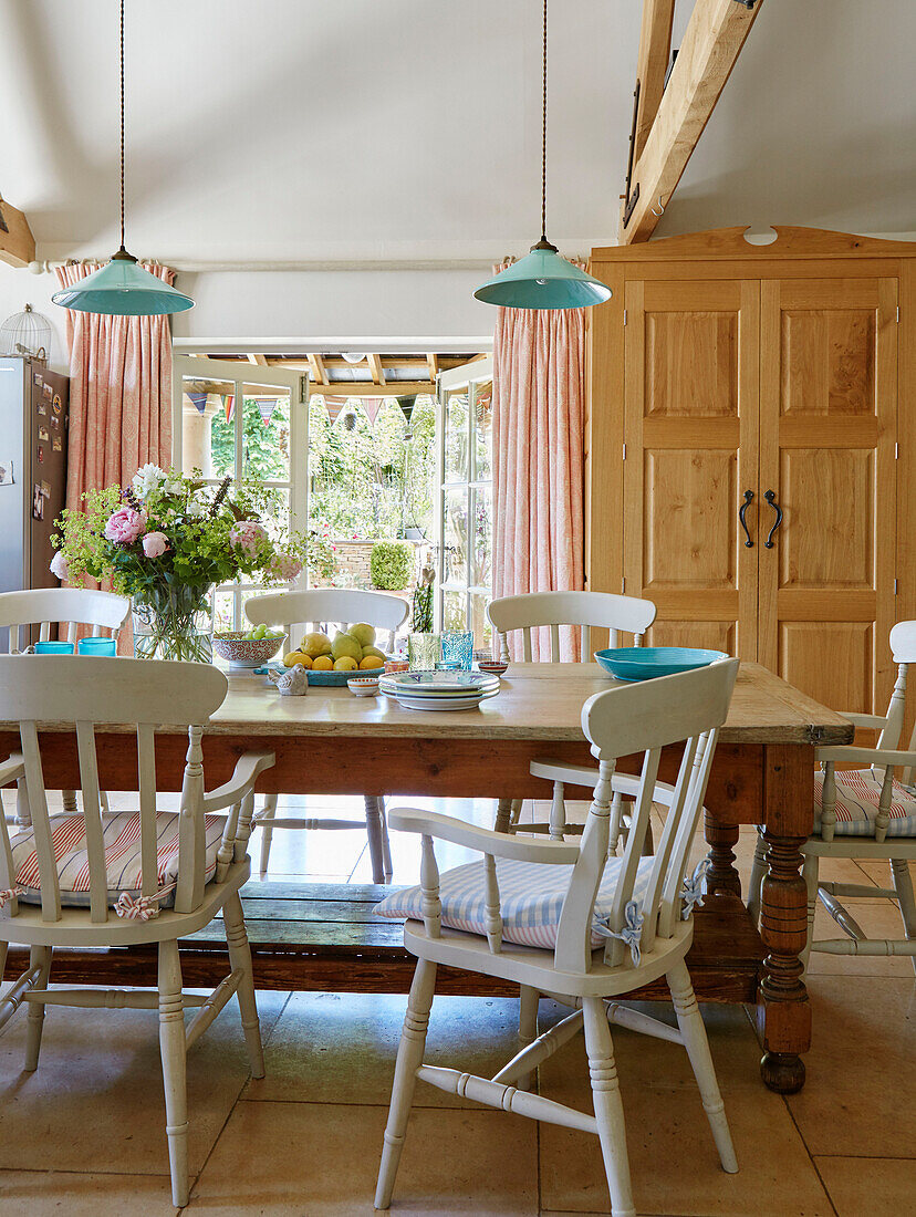 Dining table with painted chairs and wooden cabinet in Warwickshire farmhouse, UK