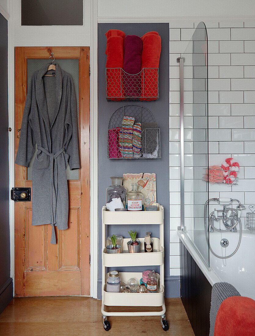 Grauer Bademantel mit orangefarbenen Handtüchern und Toilettenartikeln auf einem Regal in einem Badezimmer in Chippenham, Wiltshire, UK