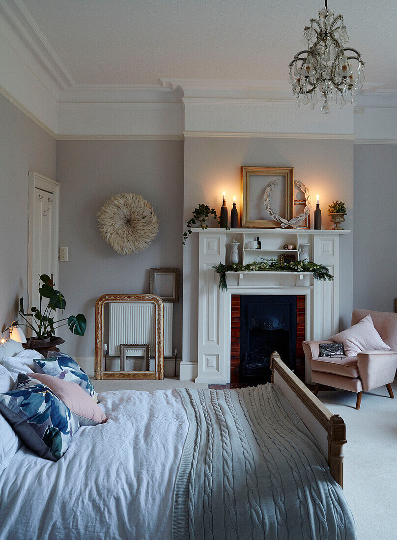 Doppelbett mit brennenden Kerzen und rosa Sessel in einem Haus in East Grinstead, West Sussex, UK