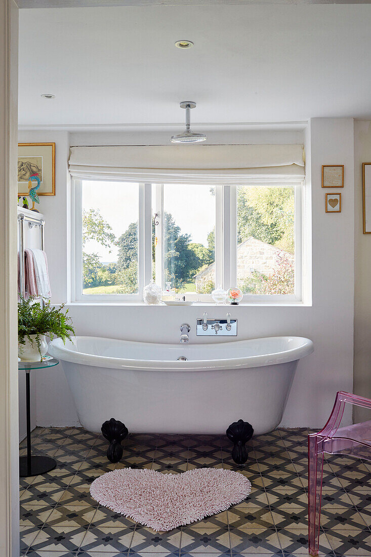 Freistehende Badewanne unter dem Fenster mit herzförmiger Matte und Pflanzenständer in einem Haus in Yorkshire, England, UK