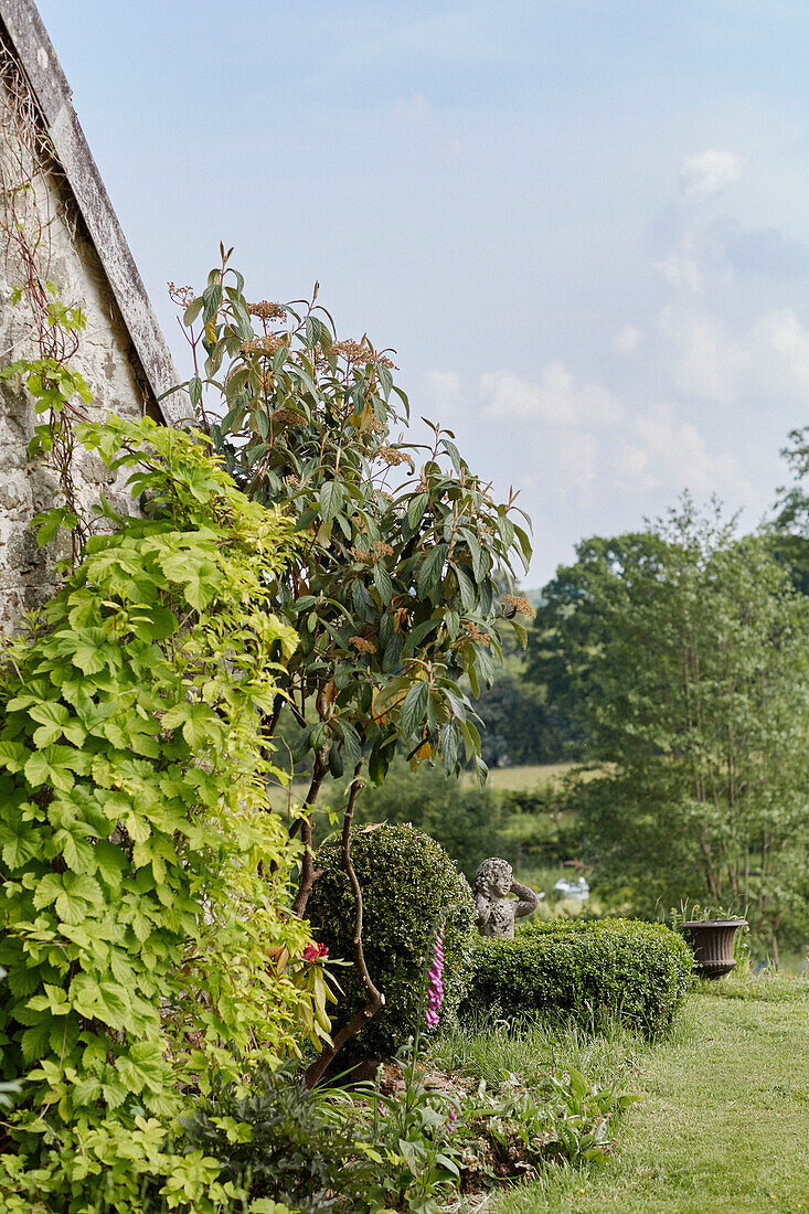 Gartenornament und Blumenbeet an der Steinfassade von einem Cottage in Powys, Wales, UK