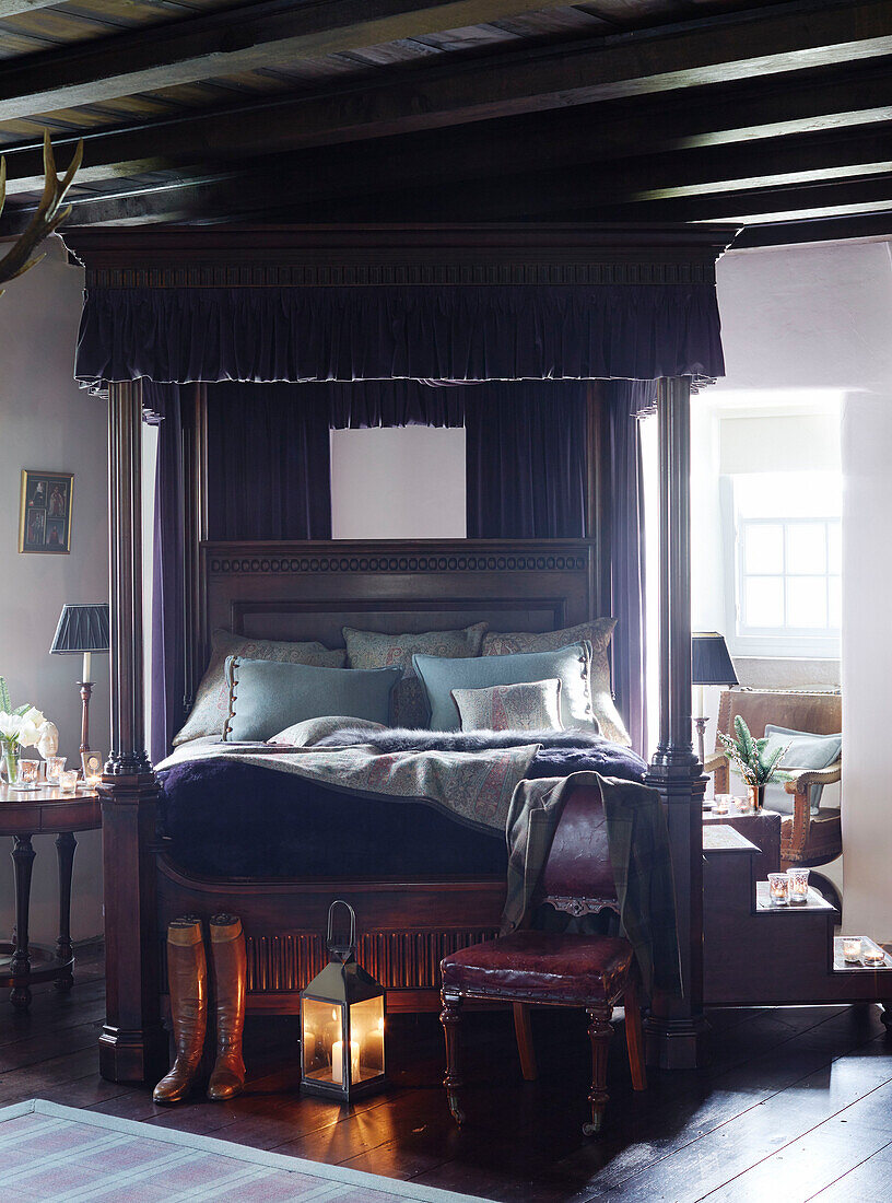 Lit lantern with riding coat and boots at foot of four poster bed in Scottish castle, UK