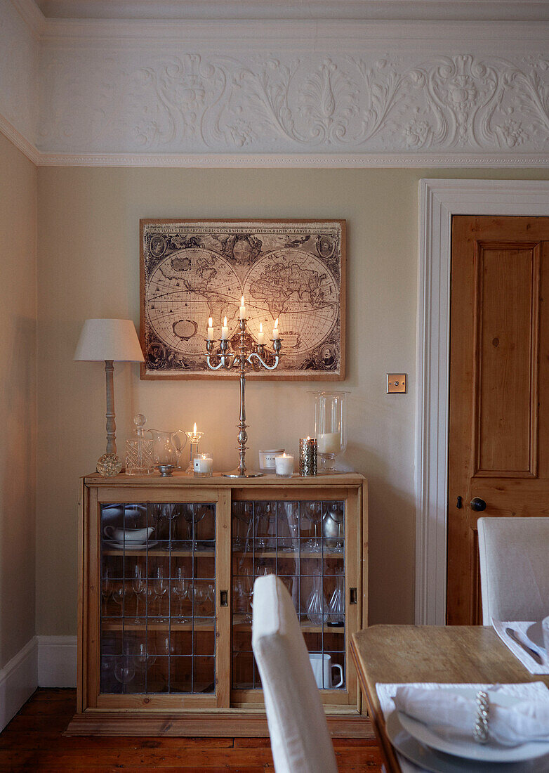 Wall map and lit candles above glass fronted display cabinet in dining room of, UK home