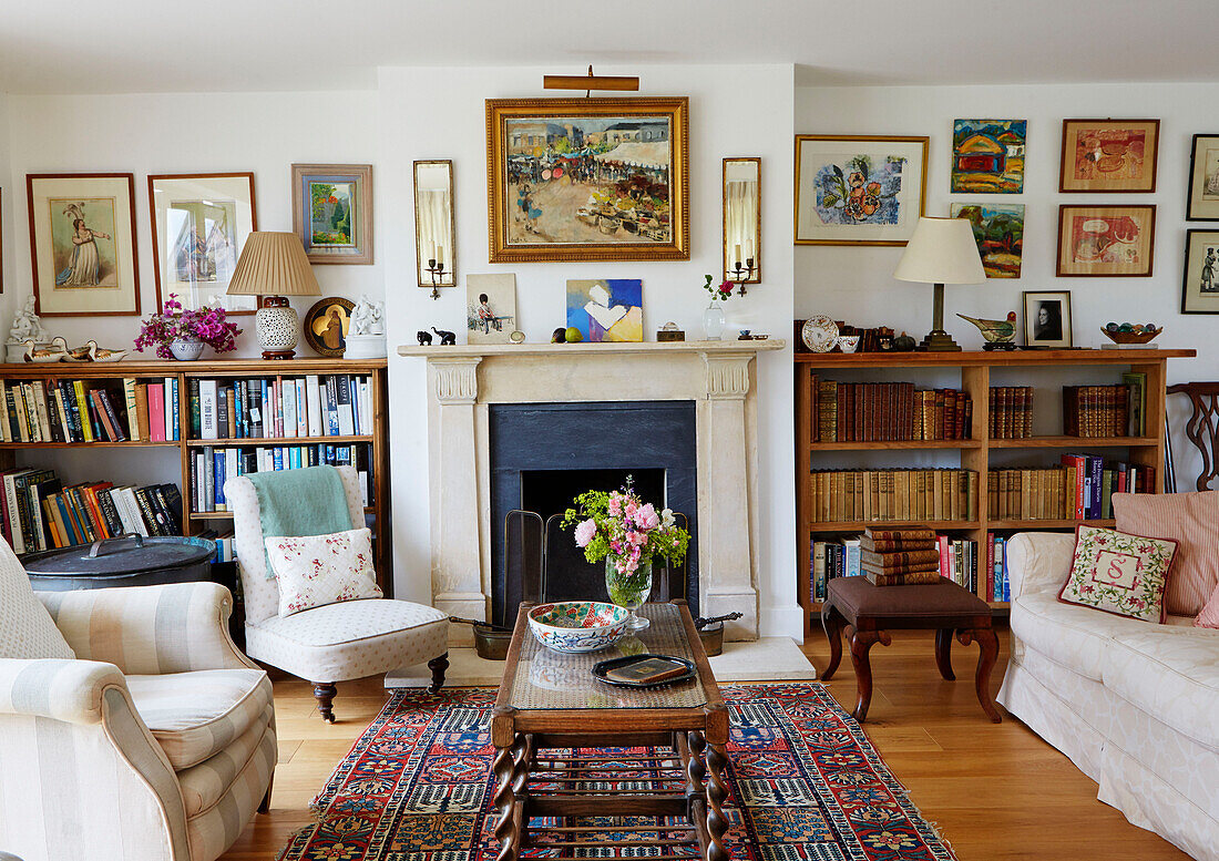 Schnittblumen auf Couchtisch mit Bücherregalen und gerahmter Kunst in einem Bauernhaus in Oxfordshire, UK