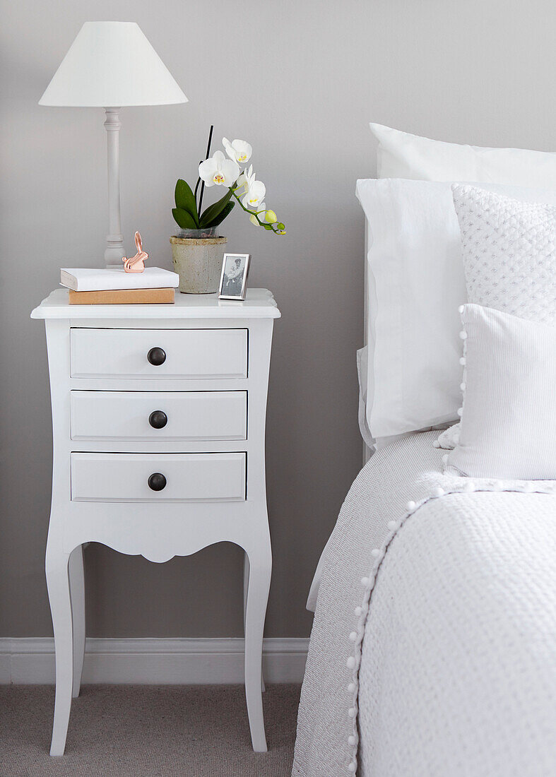 White drawers with orchid at bedside in North Yorkshire home, UK