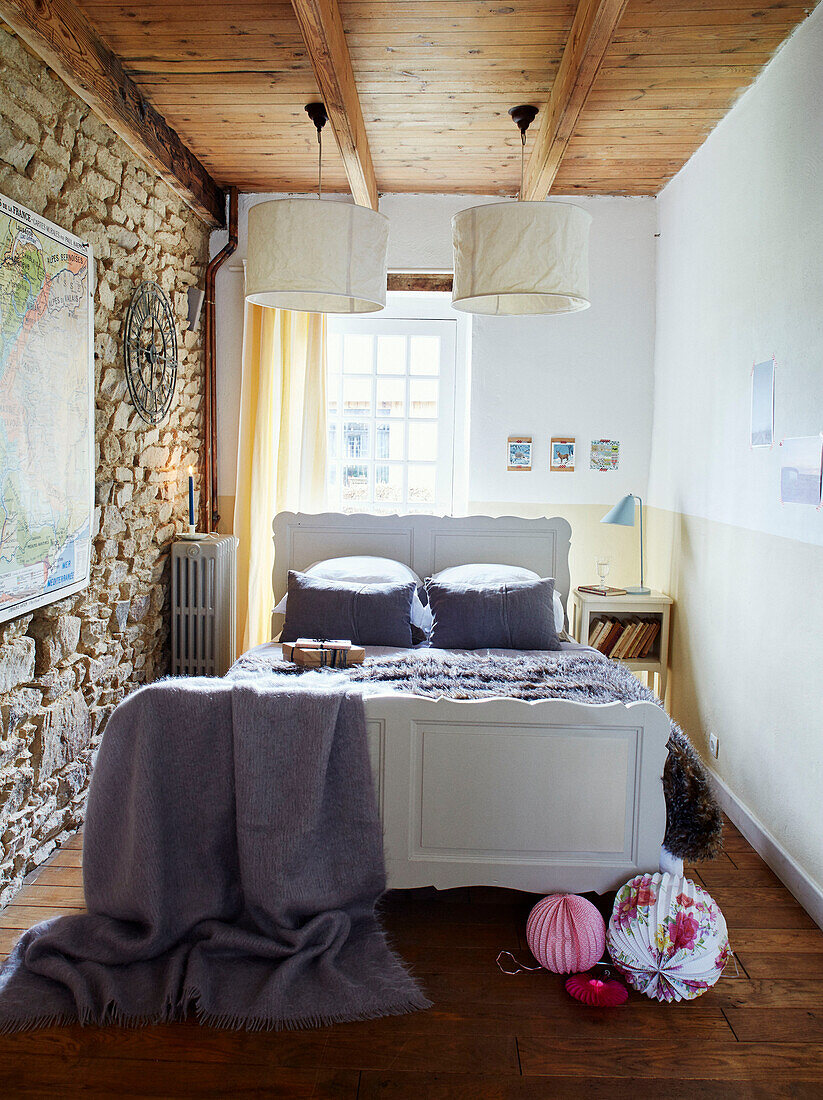 Paper shades above double bed with exposed stone wall in Brittany cottage, France