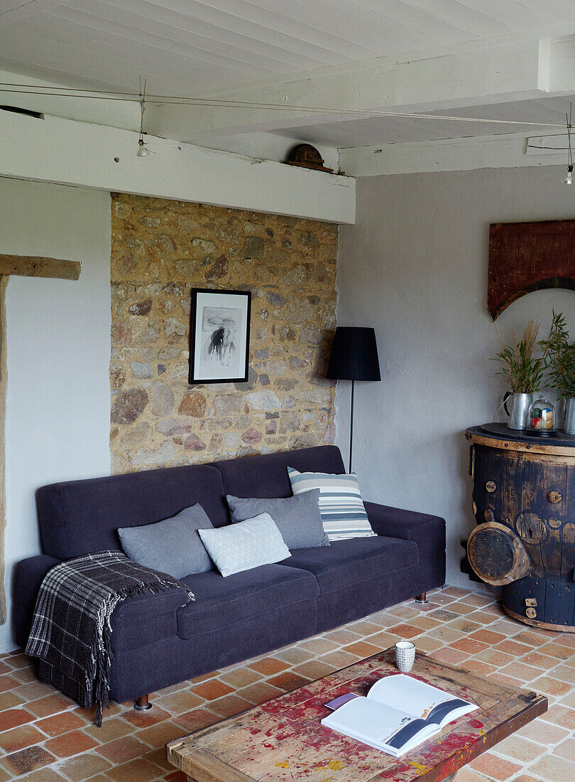 Foled blanket on purple sofa with exposed stone wall in Brittany cottage, France
