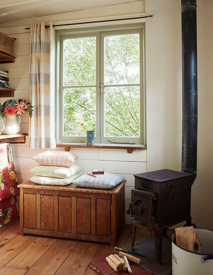 Window and trunk with cushions beside small stove inside The Majestic bus near Hay-on-Wye, Wales, UK