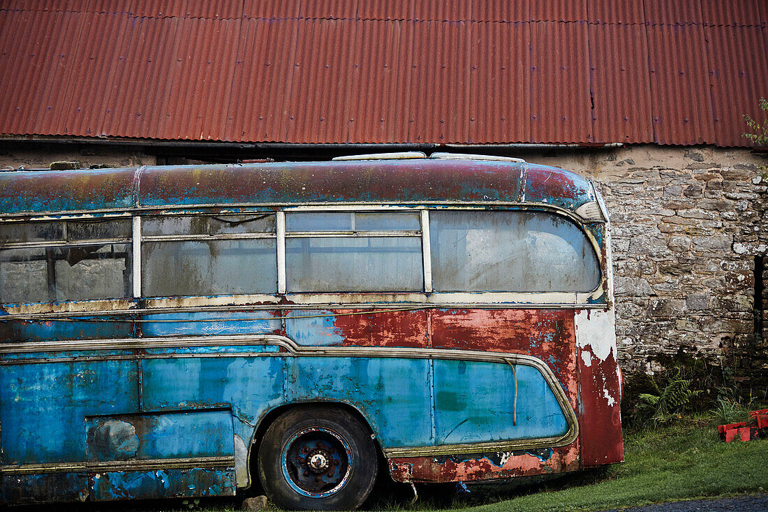 Old blue bus outside stone barn with corrugated metal roof in Radnorshire-Herefordshire border