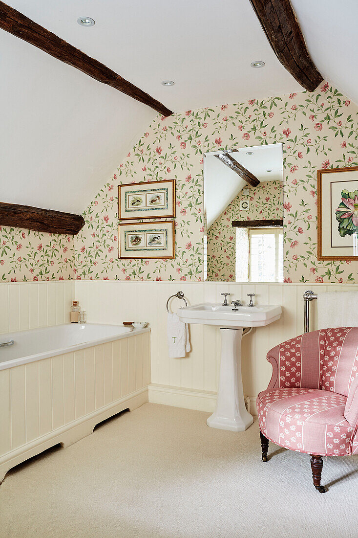 Bathroom with floral wallpaper and upholstered antique chair in Cotswolds home, UK