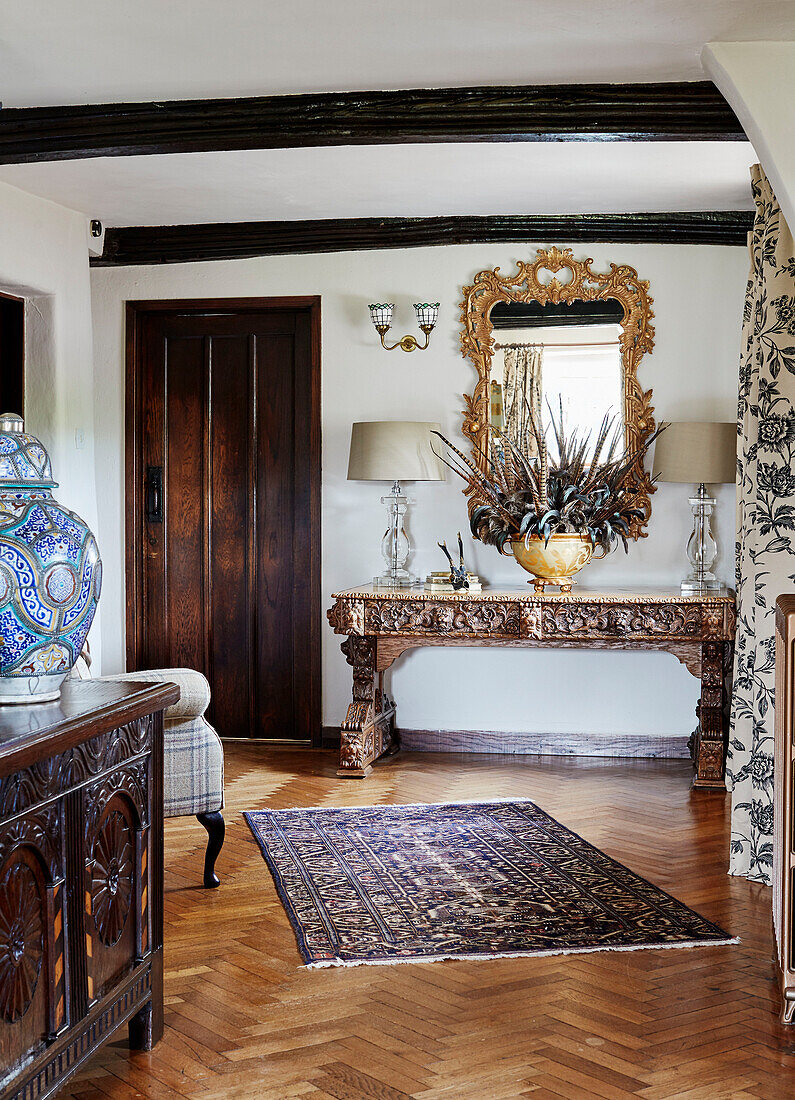 Patterned rug on parquet floor with gilt mirror above carved console in Devon home, UK