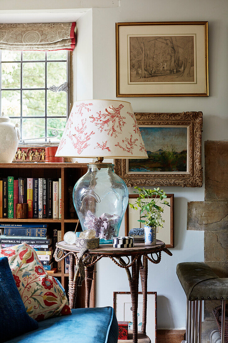 Glaslampe auf Beistelltisch mit gerahmten Bildern und Bücherregal in einem Bauernhaus in Oxfordshire, UK