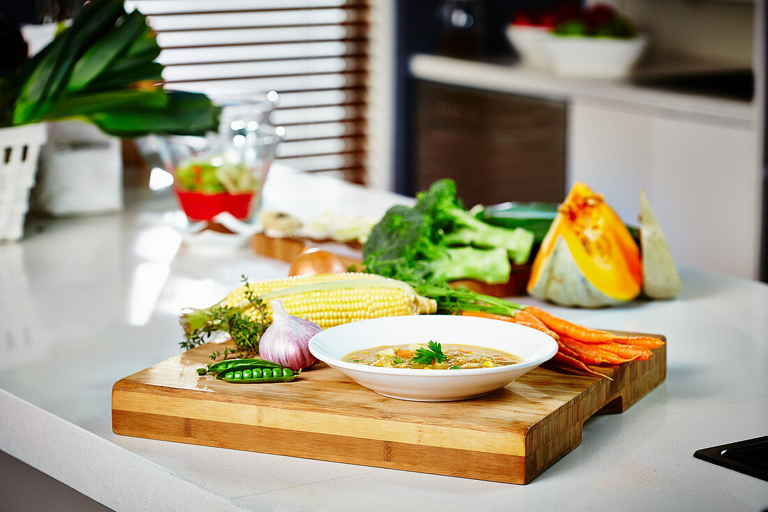 Ein Teller Gemüsesuppe auf Küchentheke umgeben von Zutaten
