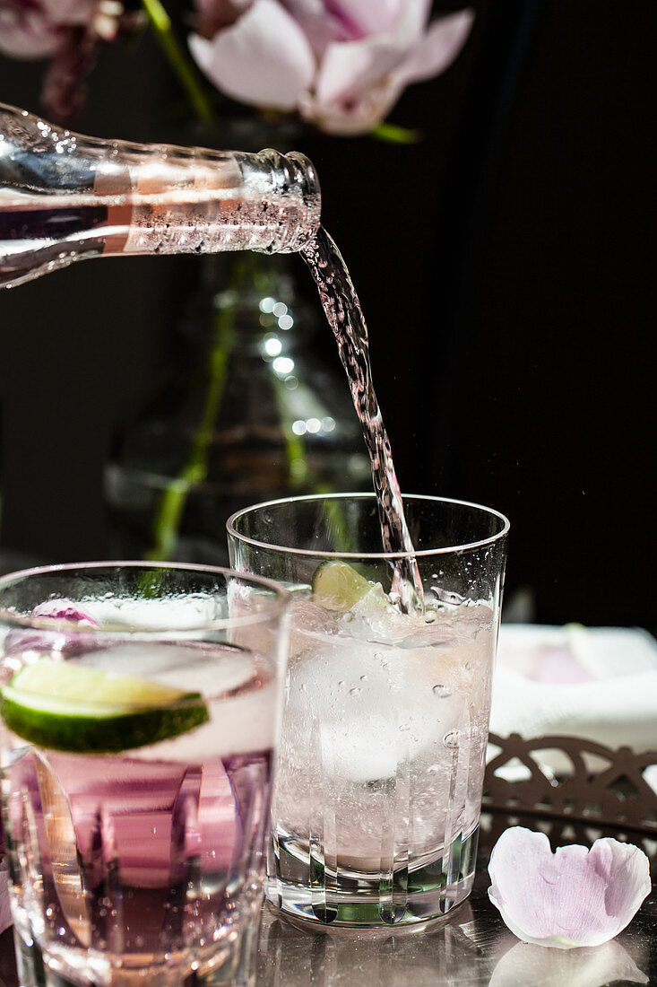 Eine Flasche rosa Tonic Water (Tonic mit Bitter) in Glas mit Gin und Limette giessen