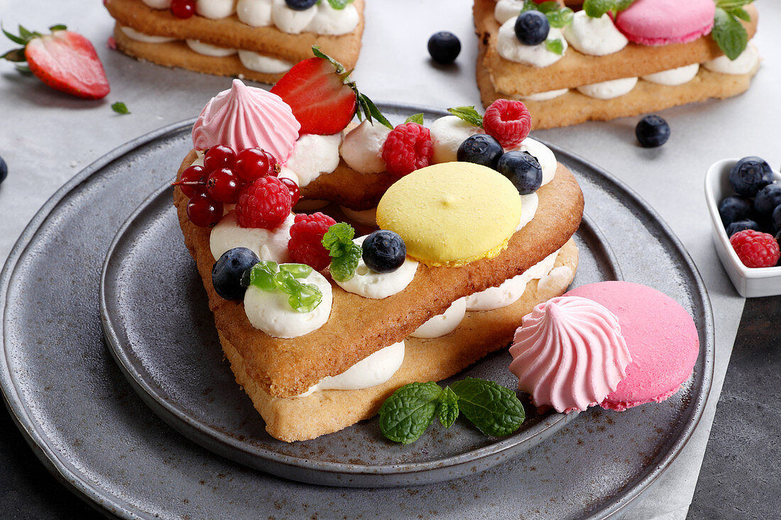 Herzförmige Kuchen mit Baiser, Obst und Macarons