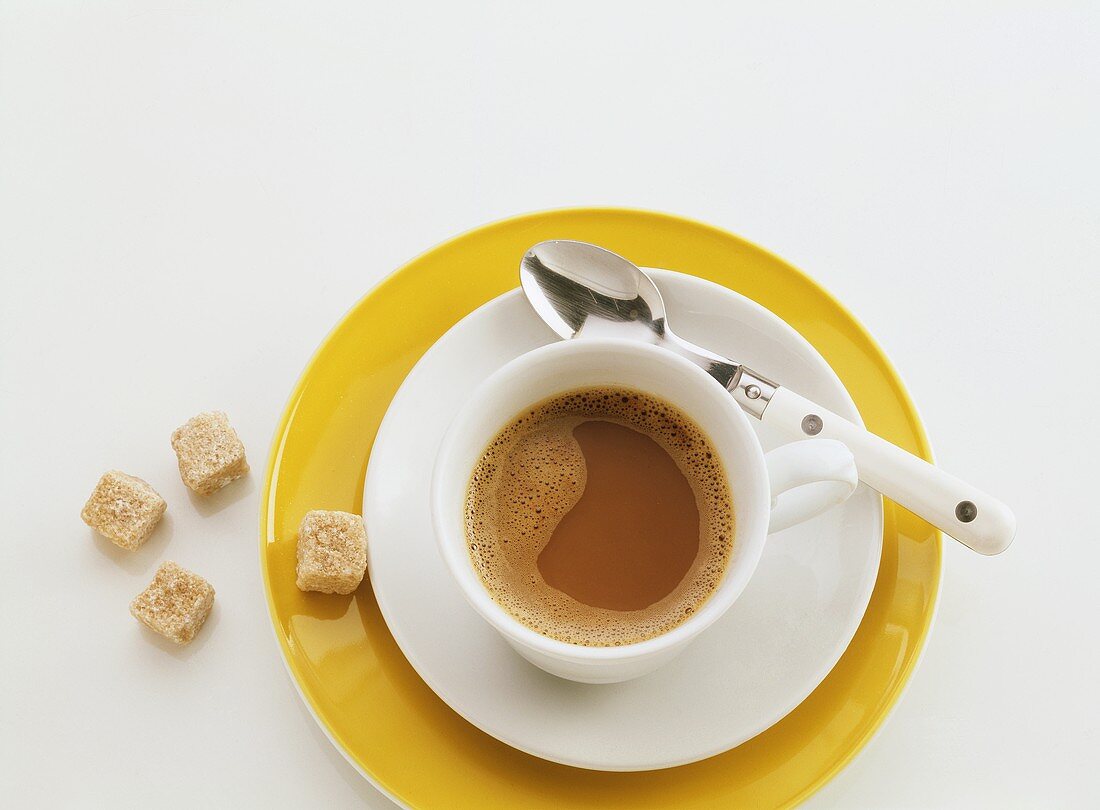 weiße Tasse Kaffee mit weißem Unterteller auf gelben Teller