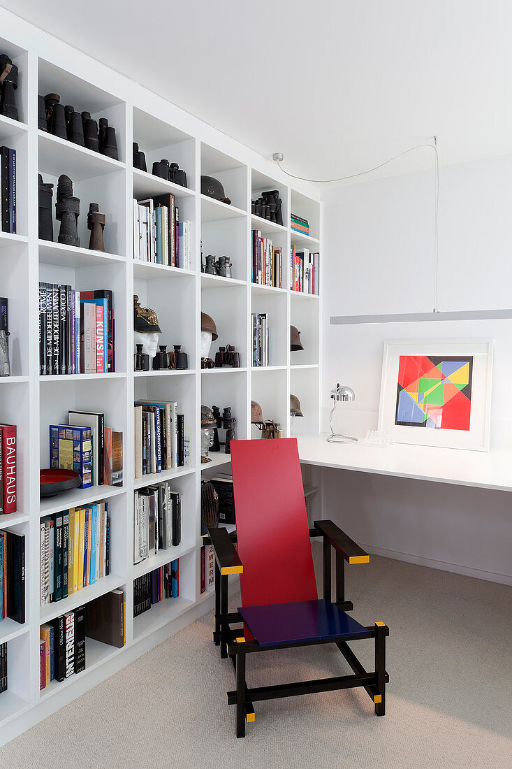 Colourful designer chair and white shelves in study