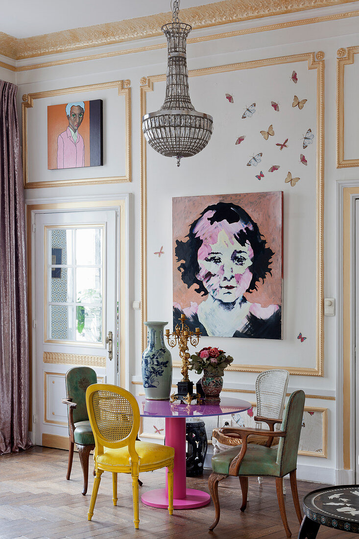 Verschiedene Stühle am pinken Tisch vor Kassettenwand mit Gemälden