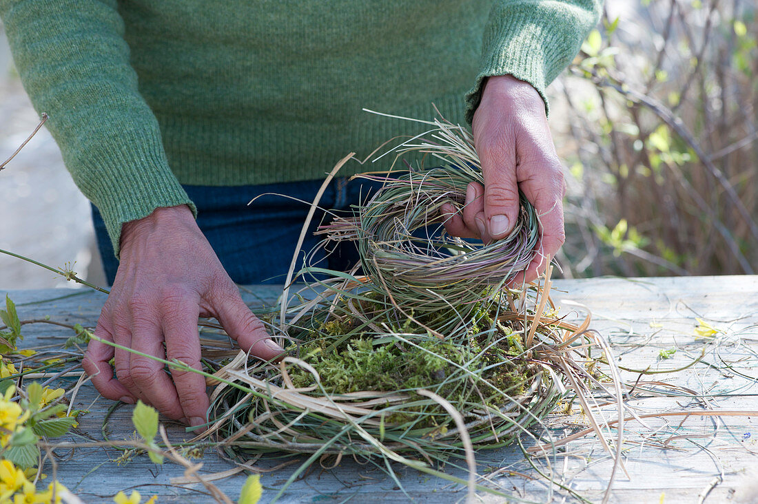 Woman winds wreath as an Easter basket made of moss and grass