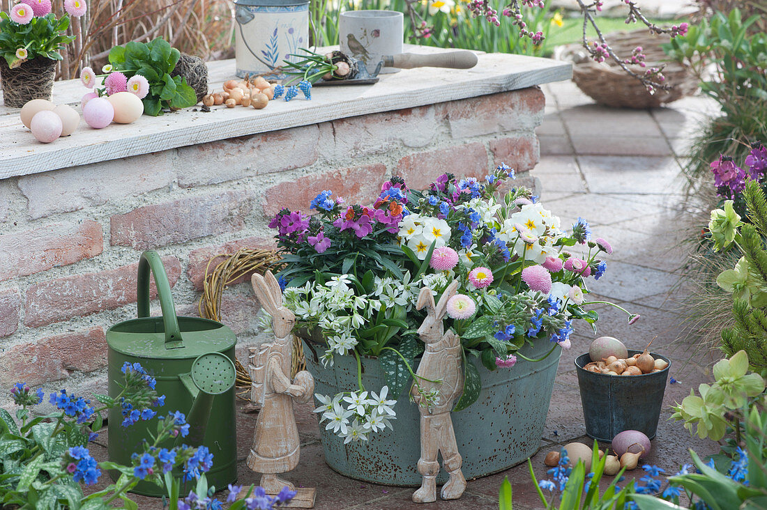 Easter terrace: sheet metal tub with gold lacquer 'Winter Orchid', milk star, primroses, honey and lungwort 'Trevi Fountain', Easter bunnies, Easter eggs and watering can