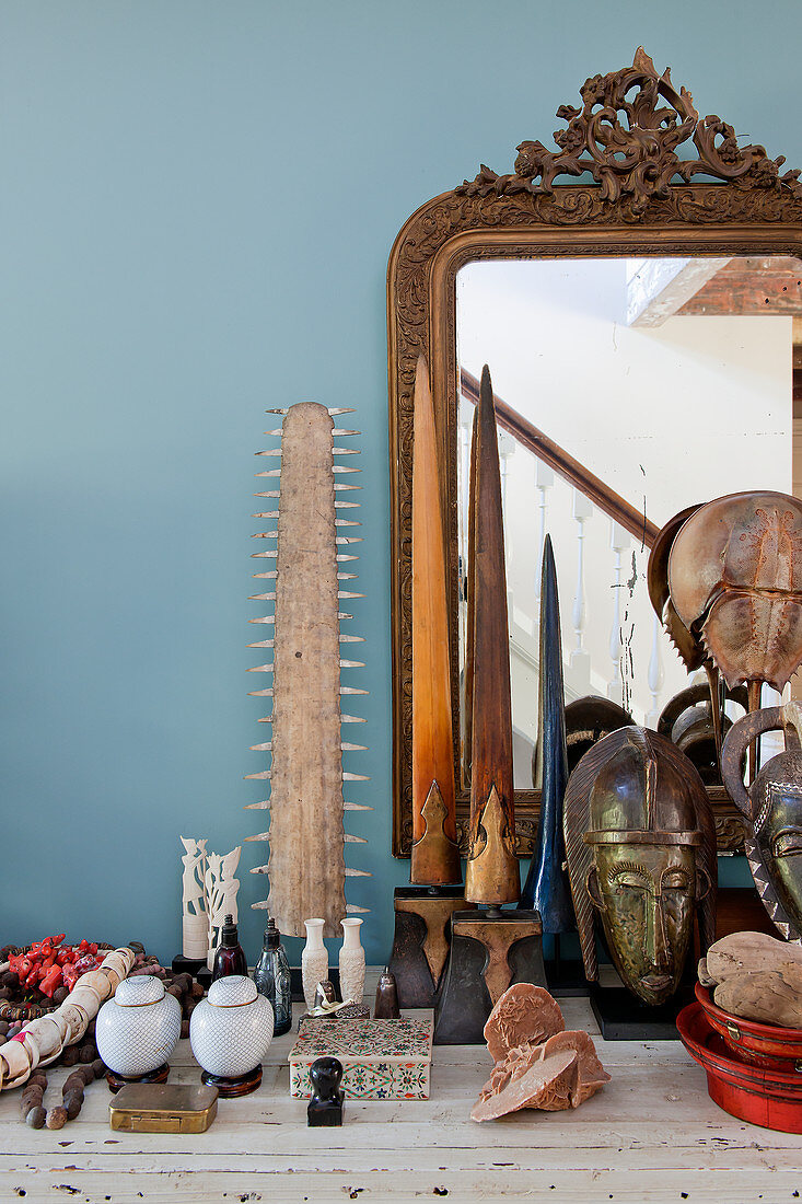 Collection of curiosities and old gilt-framed mirror against blue wall