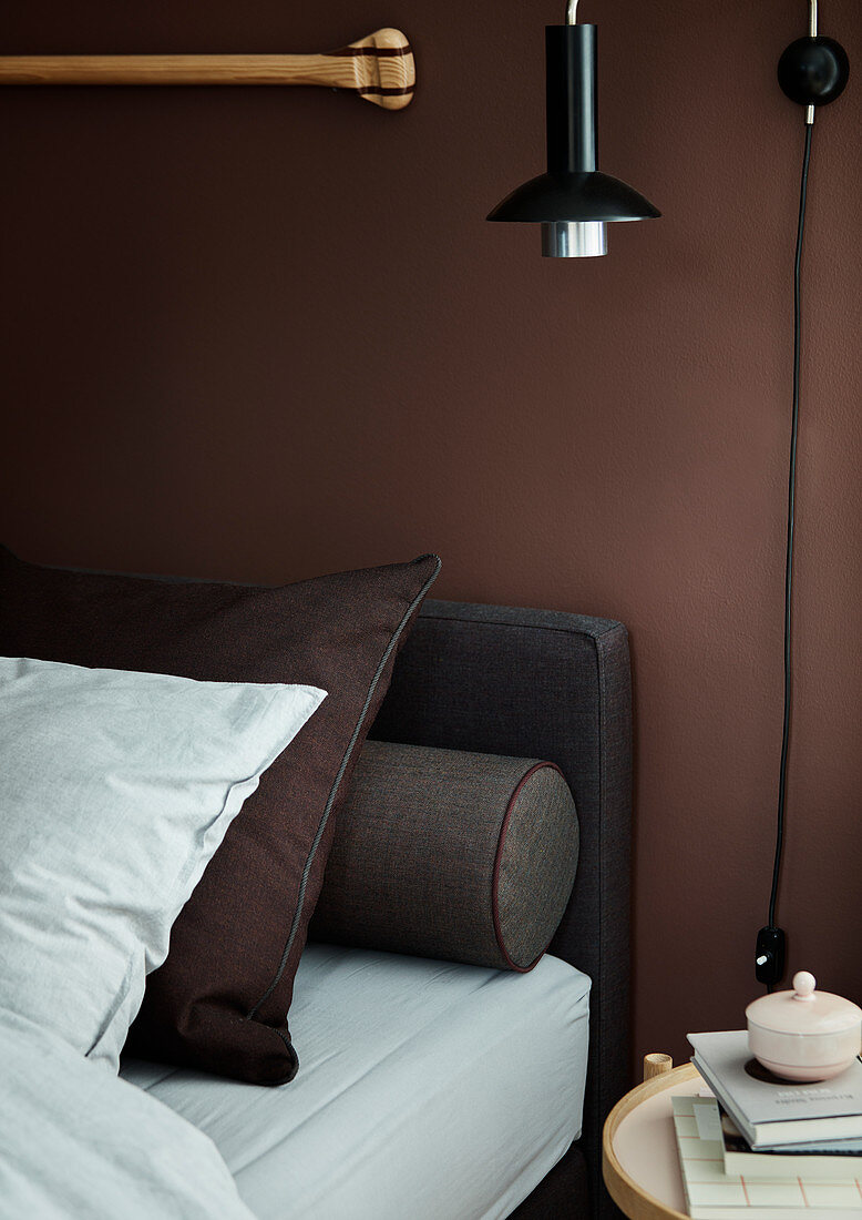 Bed with pillows and bolster against brown wall