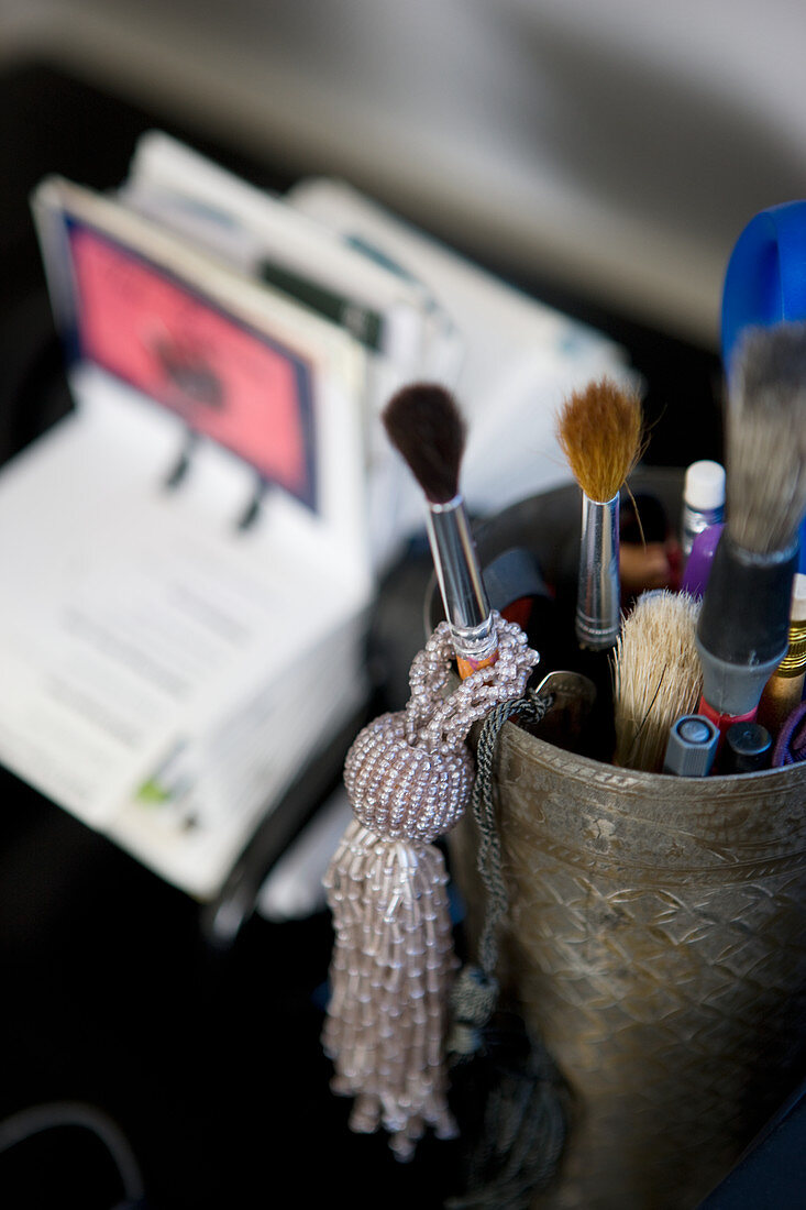 Pot of paintbrushes and beaded tassel on desk