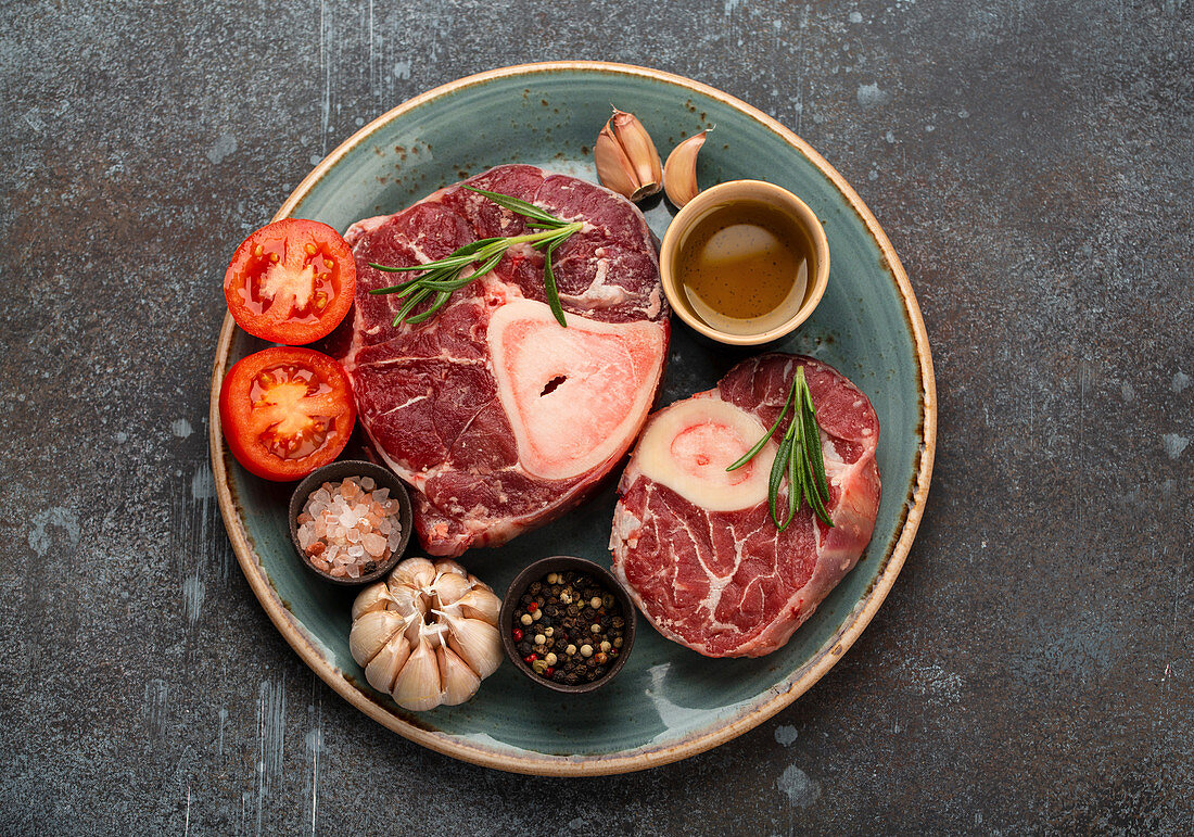 Zutaten für Ossobuco - rohe Kalbshaxe mit Gewürzen, Tomaten, Kräutern und Olivenöl