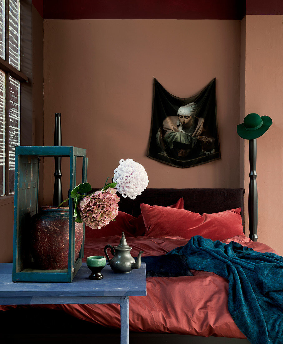 Bed against dusky pink wall with flowers on blue table in foreground