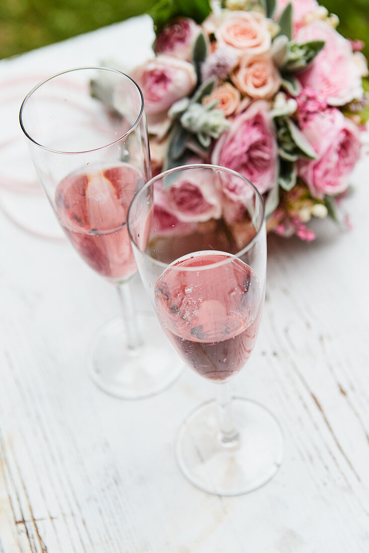 Glasses of sparkling wine in front of a bouquet of roses, lily of the valley and lamb's-ears