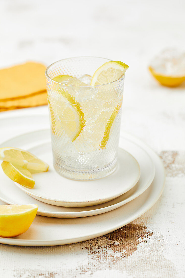 A glass of water with ice cubes and lemon wedges