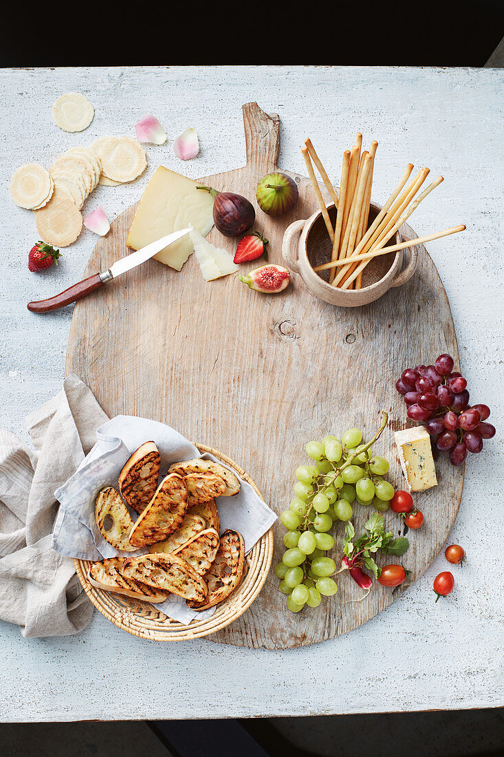 Cheese, toasted bread, breadsticks and fruits on a wooden board