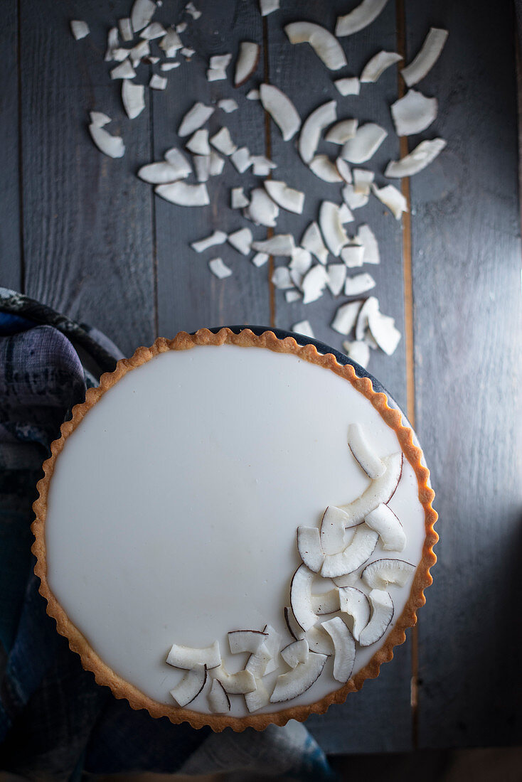 Coconut tart with coconut chips on a dark wooden surface