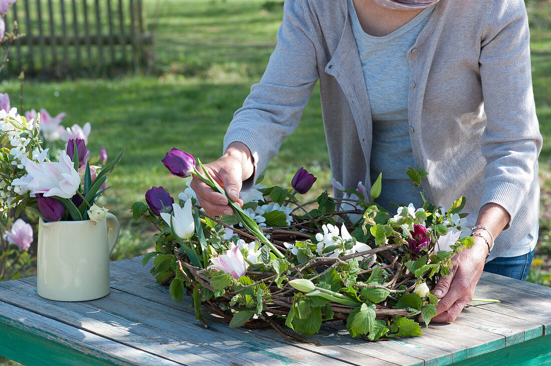 Woman puts tulips in wreath with wheel spars, tendrils and twigs