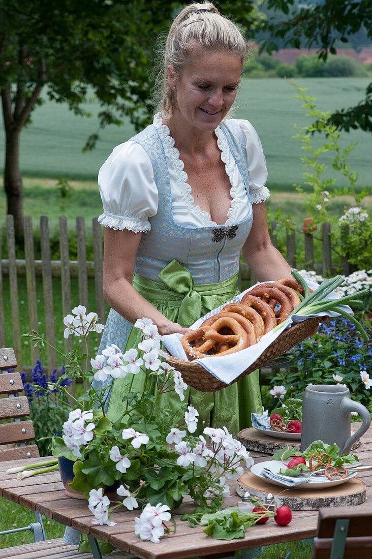 Woman sets the table for the Bavarian snack: plate with radishes and pretzels on wooden discs, beer mug