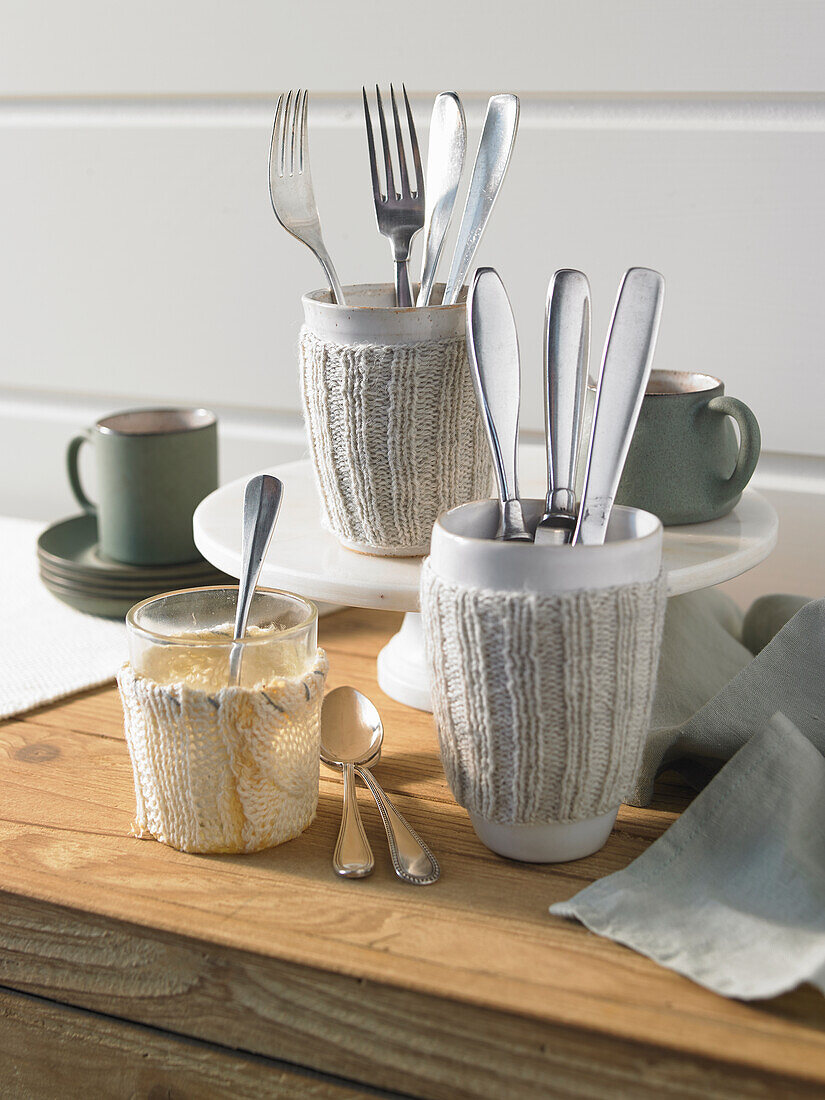 Mugs with matching colored knitted cuffs as cutlery holders