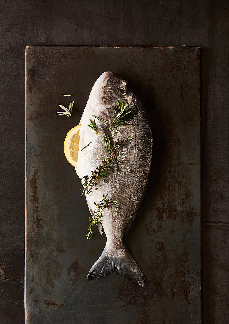 Whole raw sea bream with a lemon wedge and herbs