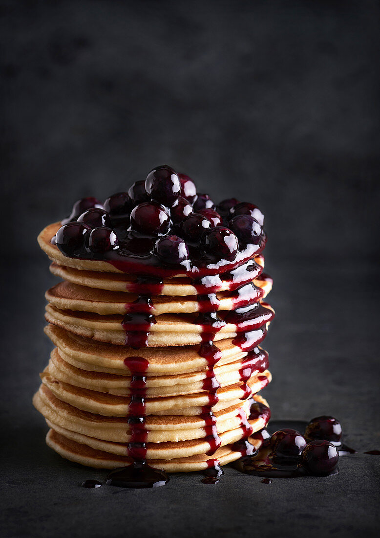 Several stacked pancakes with cherries and cherry sauce