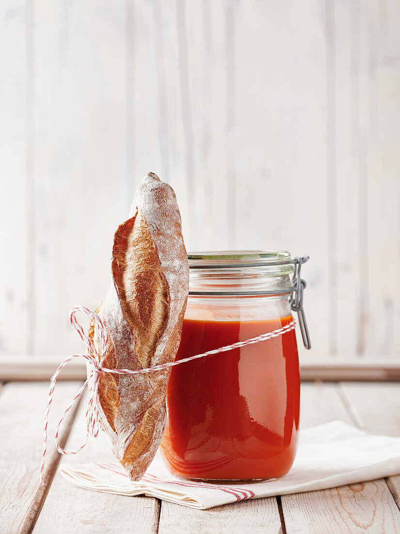 Tomato soup in a mason jar with a mini baguette on a napkin