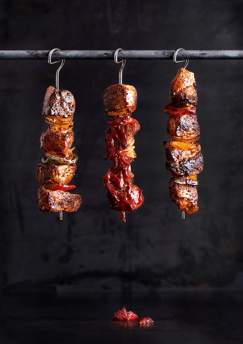 Schweinefleischspiesse mit Paprika und Zwiebeln hängen auf Metallstange