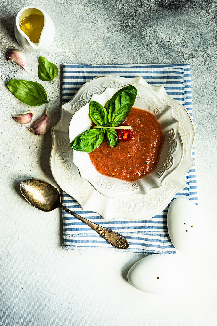 Traditional spanish tomato soup Gazpacho derved in ceranic bowl with fresh basil leaves on stone background with copy space