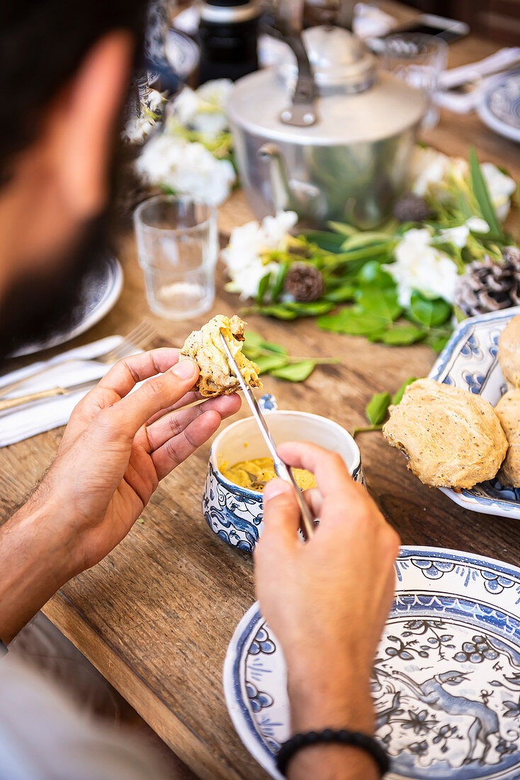 Mann bestreicht hausgemachtes Brot mit Hummus