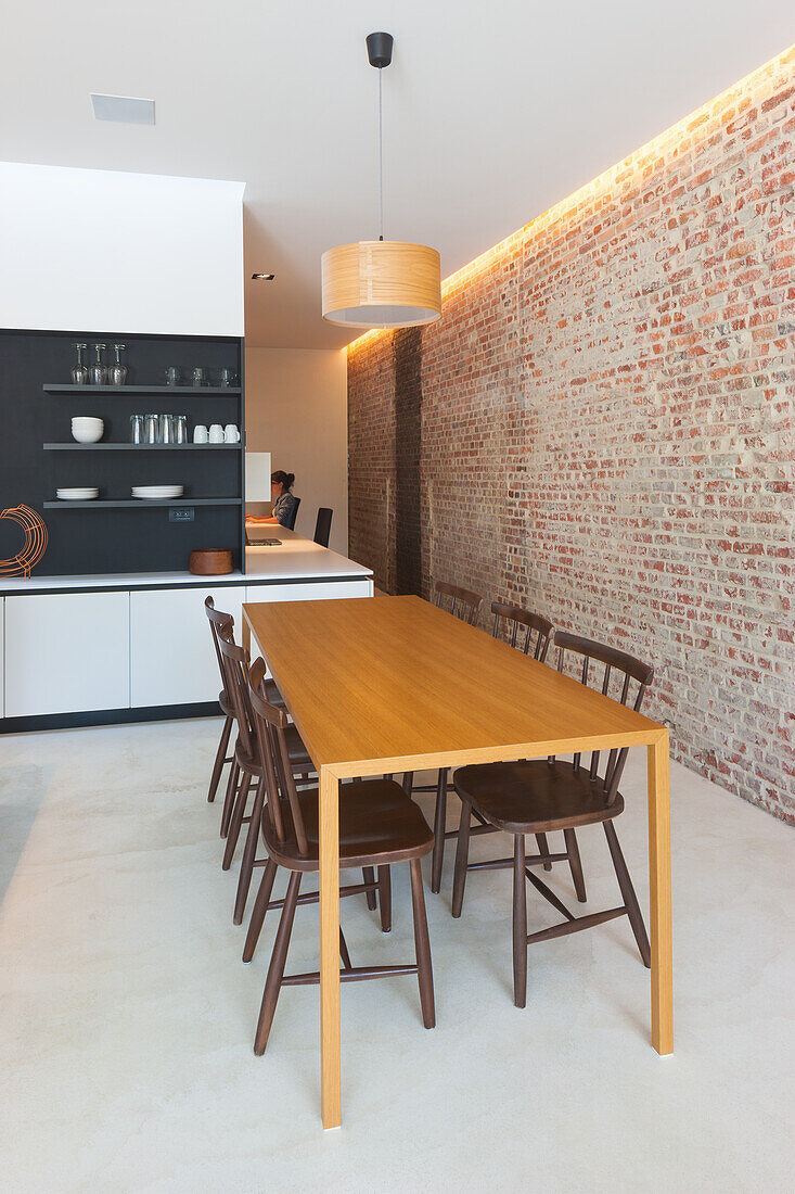 Wooden dining table and dark chairs, brick wall in modern eat-in kitchen