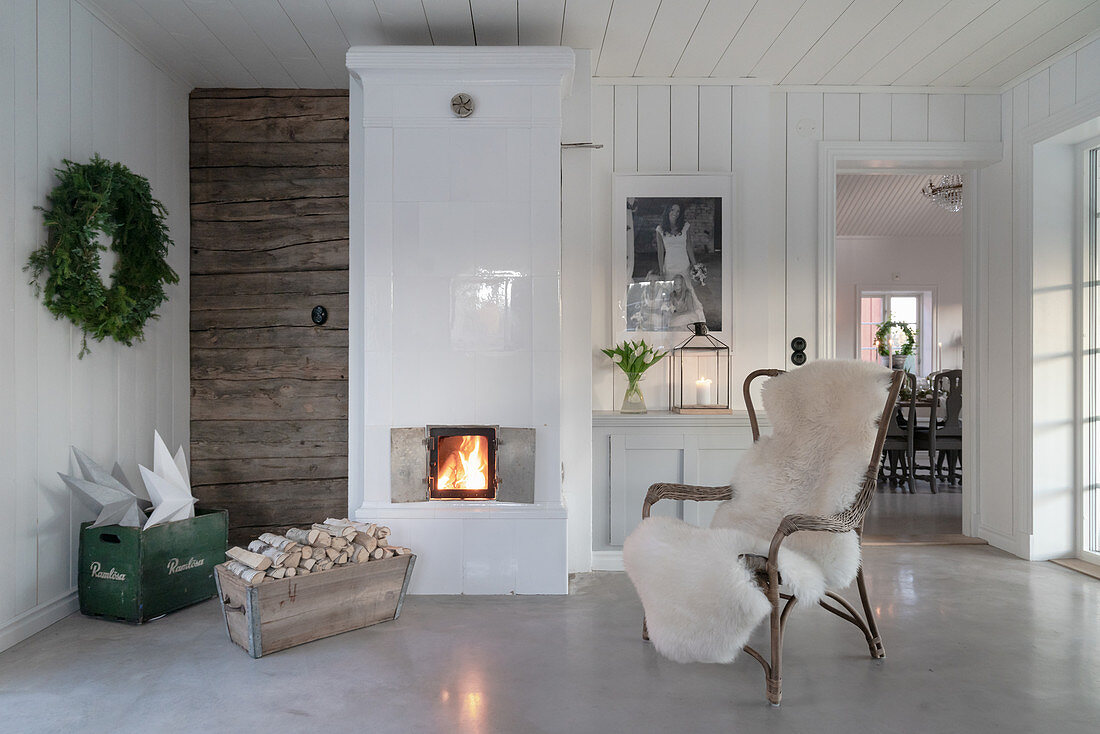 Armchair with sheepskin blanket in front of tiled stove in rustic living room