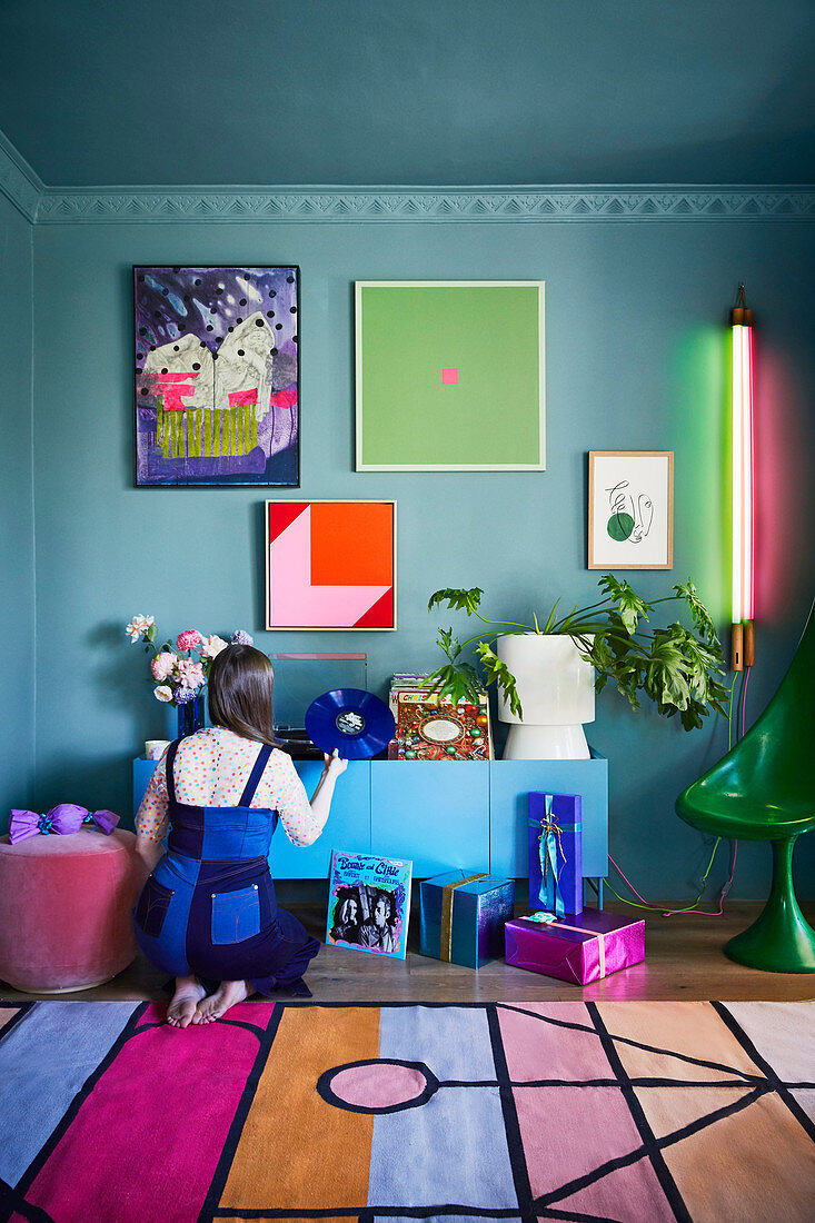 Woman kneels in front of sideboard in kitschy colourful living room
