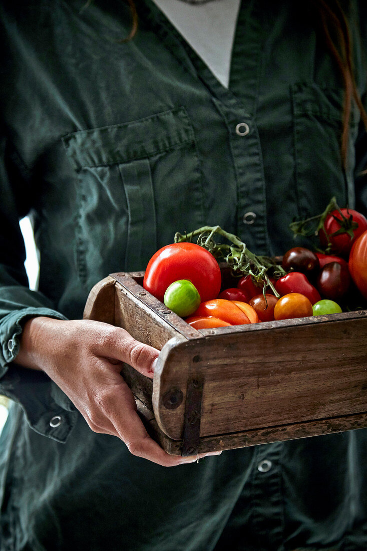 Woman holding wooden box with colorful tomatoes