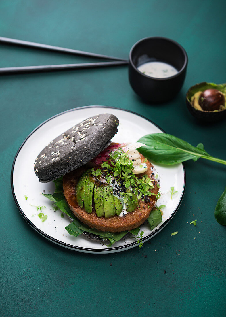 Soja-Weizenprotein-Bratling mit Avocado, Radieschen und zweierlei Saucen im schwarzen Burgerbrötchen