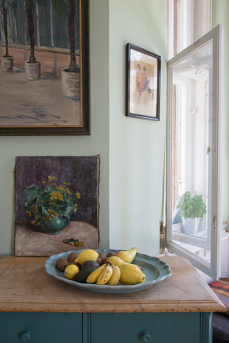 Obstschale und Blumenbild auf einer alten Kommode am Fenster