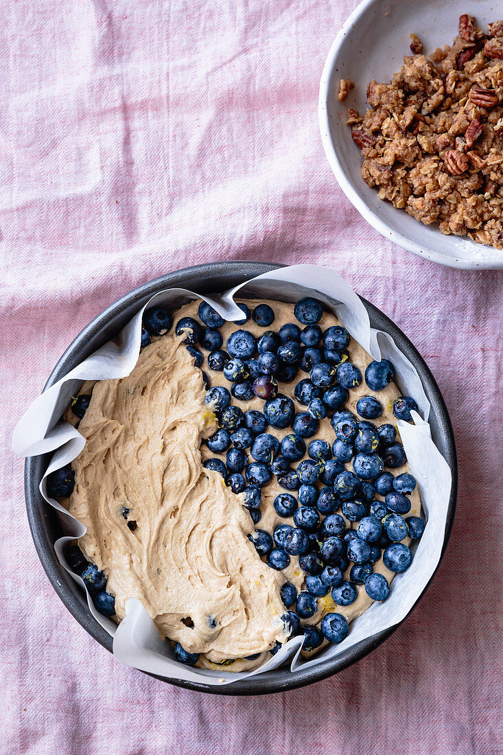 Blueberries on blueberry coffee cake batter beside pecan streusel in a bowl.